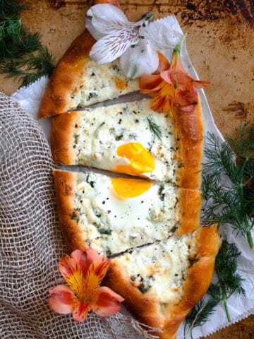 A khachapuri bread boat filled with herbed cheese and an egg, cut into slices.