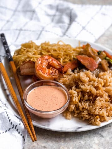 Yum Yum sauce sitting on a plate of hibachi food with chopsticks.