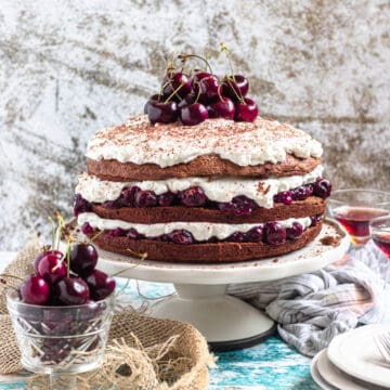 German Black Forest Cake surrounded by cherries, serving plates, and liquor.