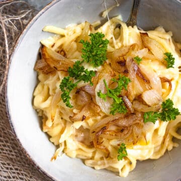 A large bowl of cheese spaetzle topped with melted cheese, sauteed onions, and parsley.
