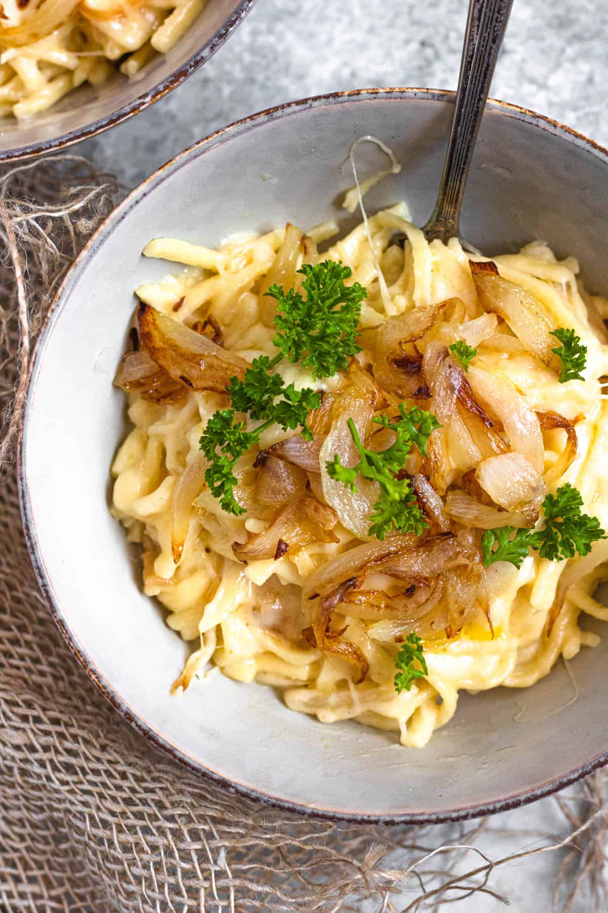 A large bowl of cheese spaetzle topped with melted cheese, sauteed onions, and parsley.