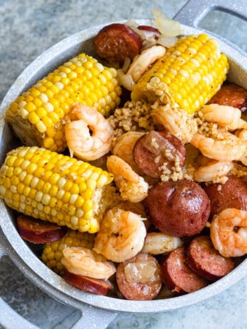 A large pot filled with shrimp, potatoes, corn cobs, sausage, and garlic.