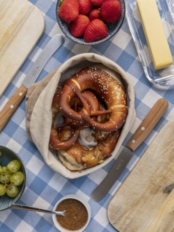 German pretzels on a gingham picnic blanket with mustard and grapes nearby.