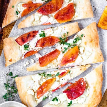 Goat cheese flatbread on a cookie sheet with parchment paper, peaches, honey and thyme.