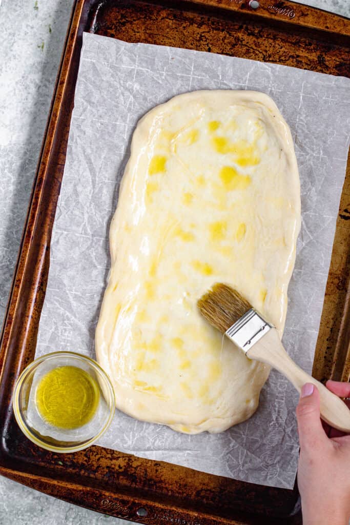 brushing olive oil on pizza dough with a pastry brush 