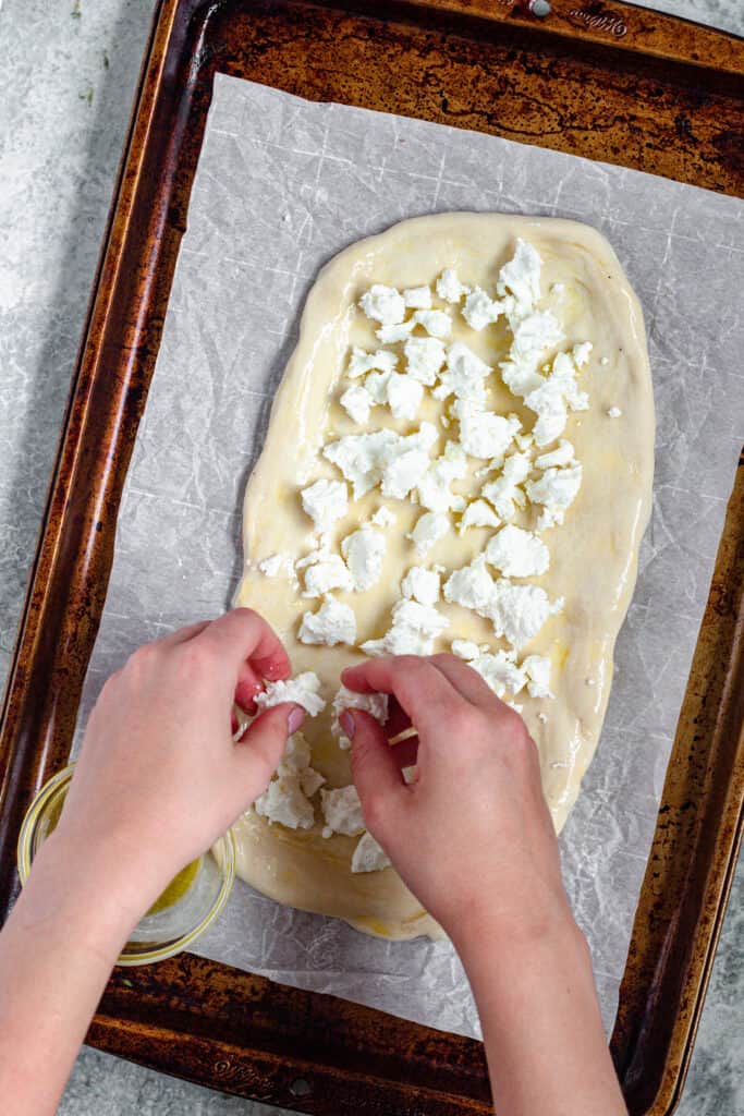 Hands crumbling goat cheese over pizza dough 