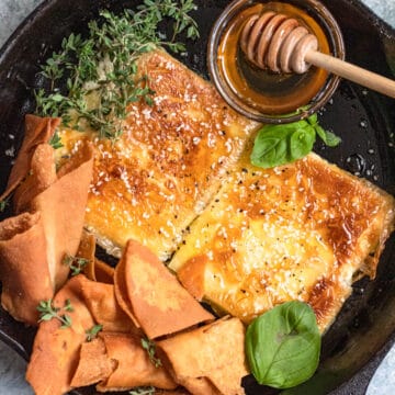 Fried feta in a cast iron skillet topped with honey next to pita chips.