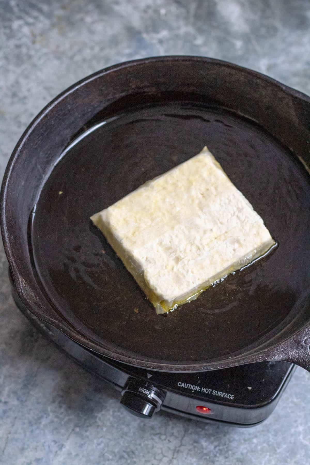 uncooked feta cheese in oil in a cast iron skillet