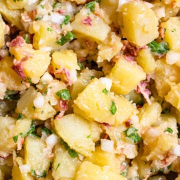German Potato salad with red onions, fresh herbs, dressing, and golden potatoes.