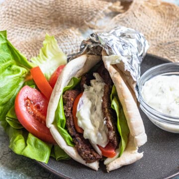 A gyro on a black plate topped with gyro meat, vegetables, and tzatziki sauce.