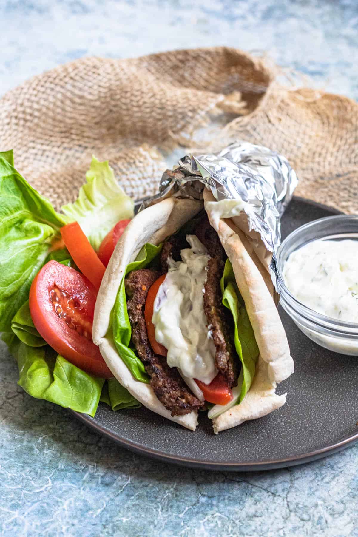 A gyro on a black plate topped with gyro meat, vegetables, and tzatziki sauce.