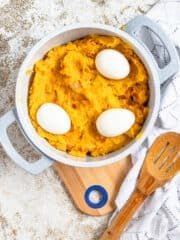 A large pot filled with sweet potatoes and topped with hard boiled eggs, surrounded by linens and a wooden spoon.