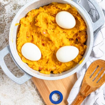 A large pot filled with sweet potatoes and topped with hard boiled eggs, surrounded by linens and a wooden spoon.