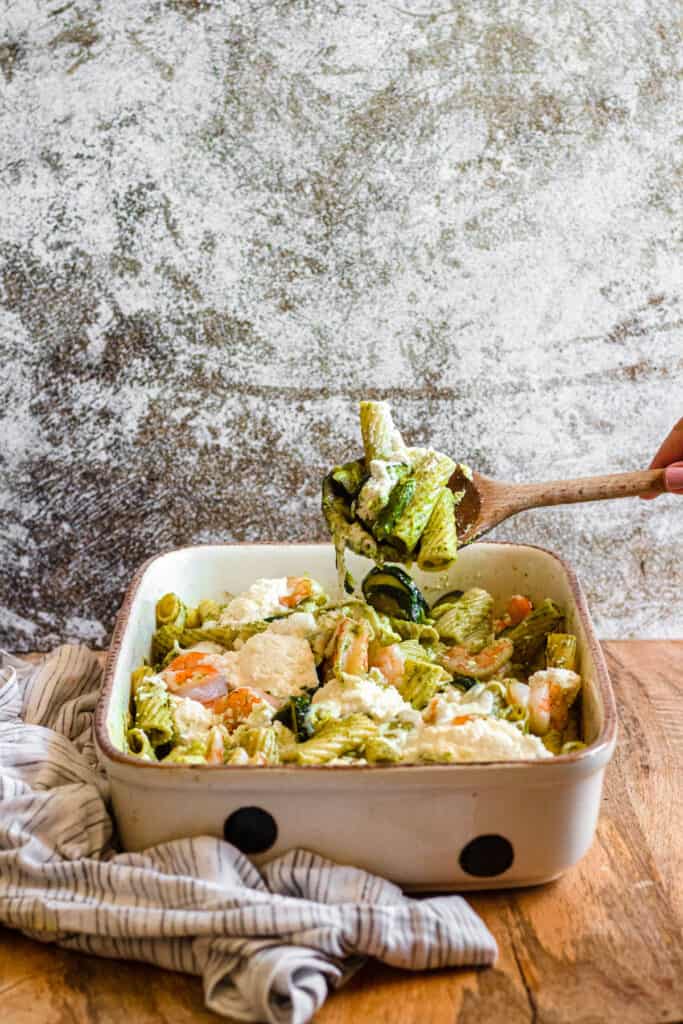 A wooden spoon scooping the shrimp and ricotta pasta bake from a baking dish.