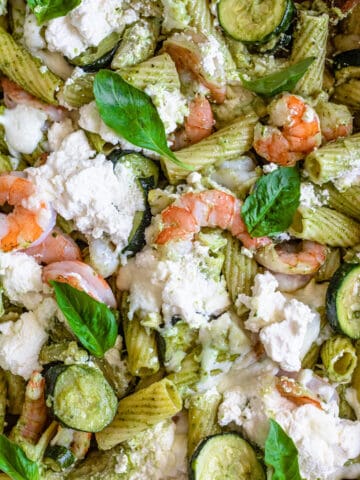 A close up of noodles, zucchini, ricotta cheese, basil, pesto, and shrimp.