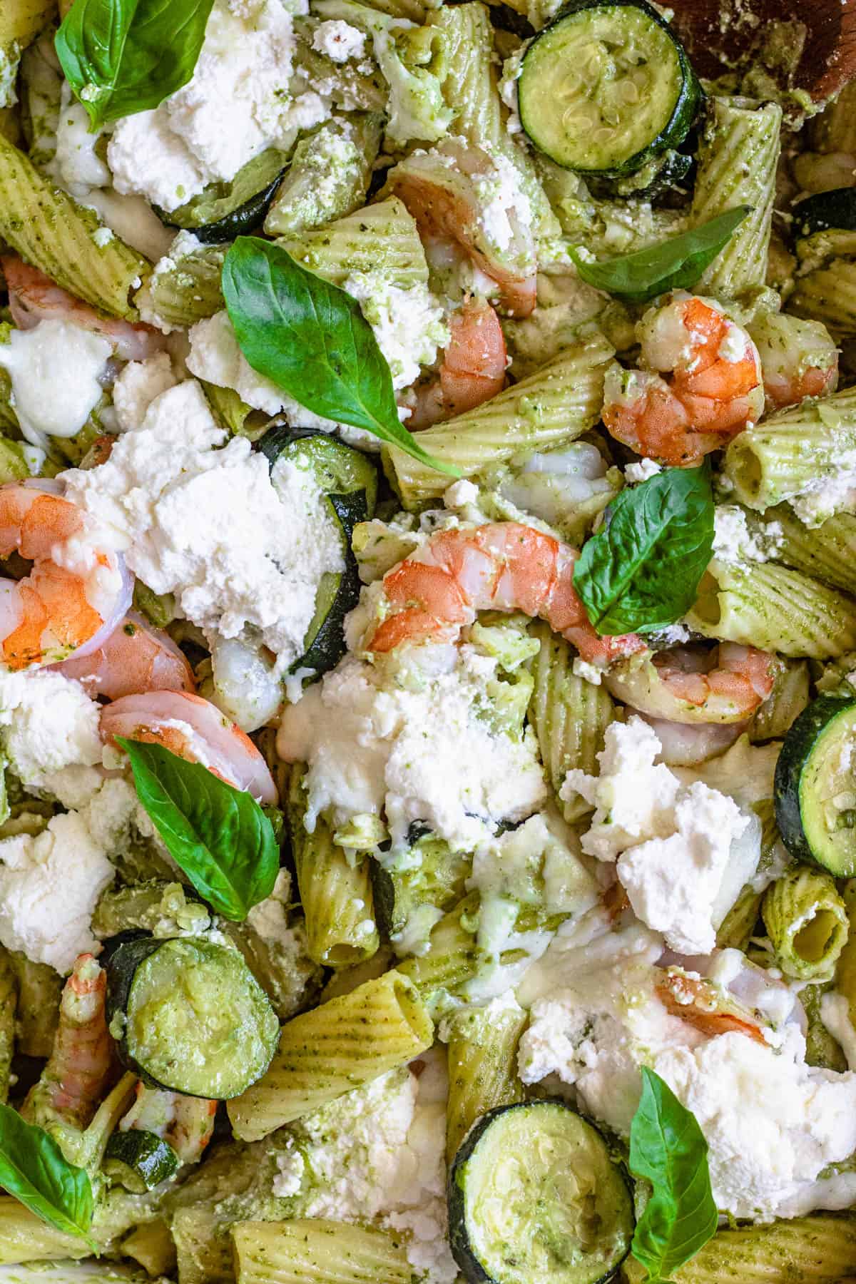 A close up of noodles, zucchini, ricotta cheese, basil, pesto, and shrimp.