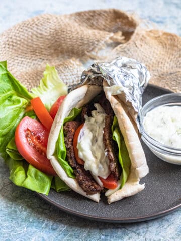 A gyro on a plate topped with vegetables and tzatziki sauce.
