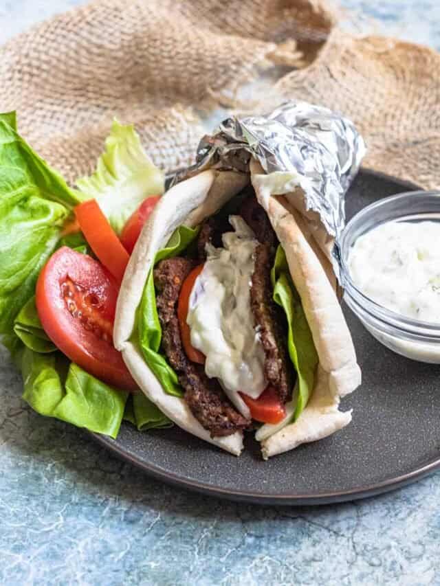A gyro sitting on a plate with a side of tzatziki sauce in a small bowl. 