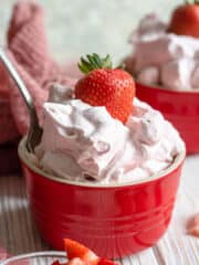 A large bowl of strawberries and cream with a strawberry sticking out of the top.
