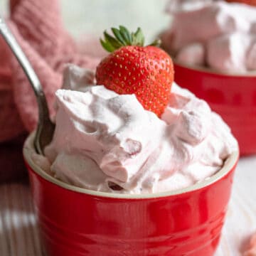 A large bowl of strawberries and cream with a strawberry sticking out of the top.