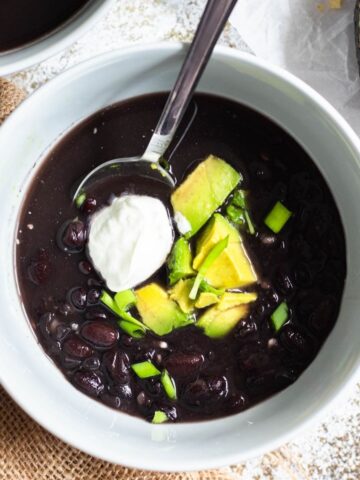 A bowl of black bean soup topped with avocado cubes and sour cream.