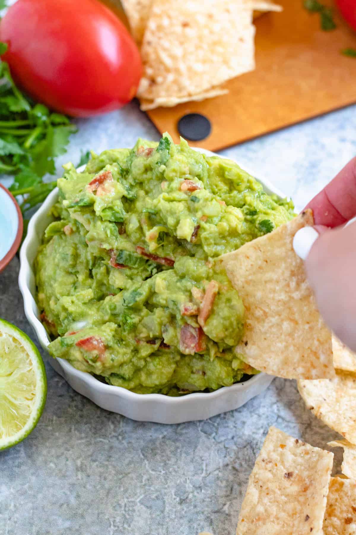 Hand holding a chip to scoop guacamole 