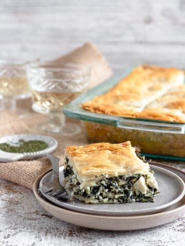A piece of spanakopita on a stack of plates with a fork next to it.