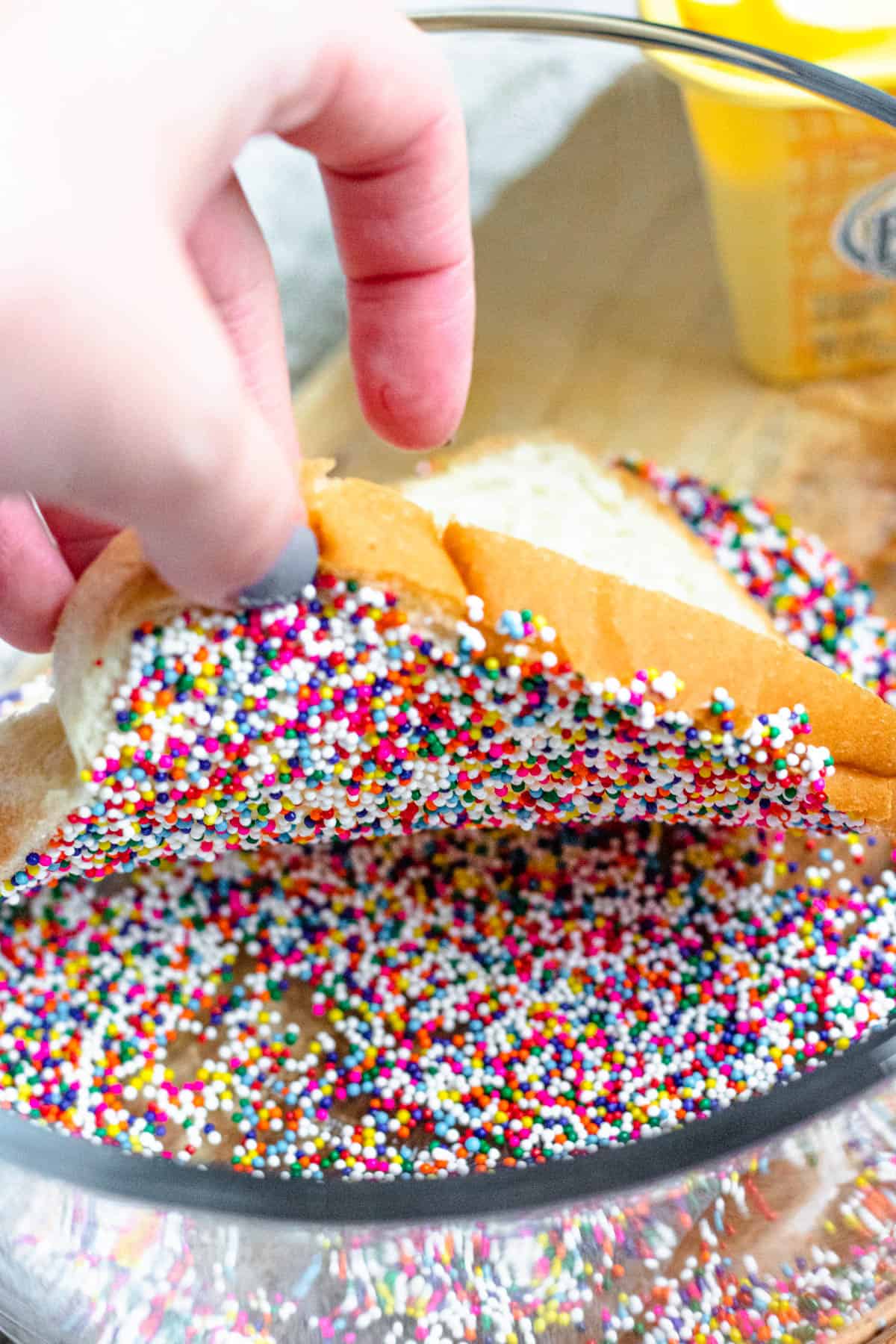 Hand lifting a slice of bread out of a bowl of sprinkles