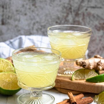 Two glasses of ginger drink with limes and cinnamon sticks.