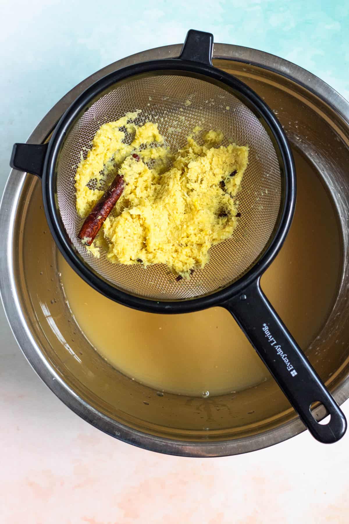 strained ginger drink with solids in a strainer and liquid in a large bowl 