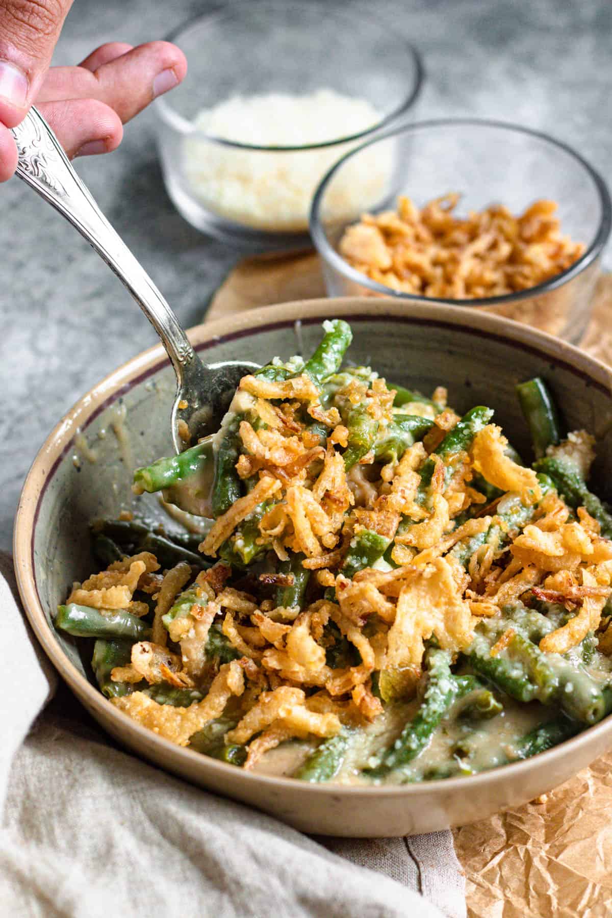Hand spooning green bean casserole out of a bowl 