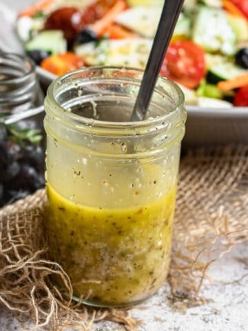 Italian dressing in a mason jar in front of a salad.
