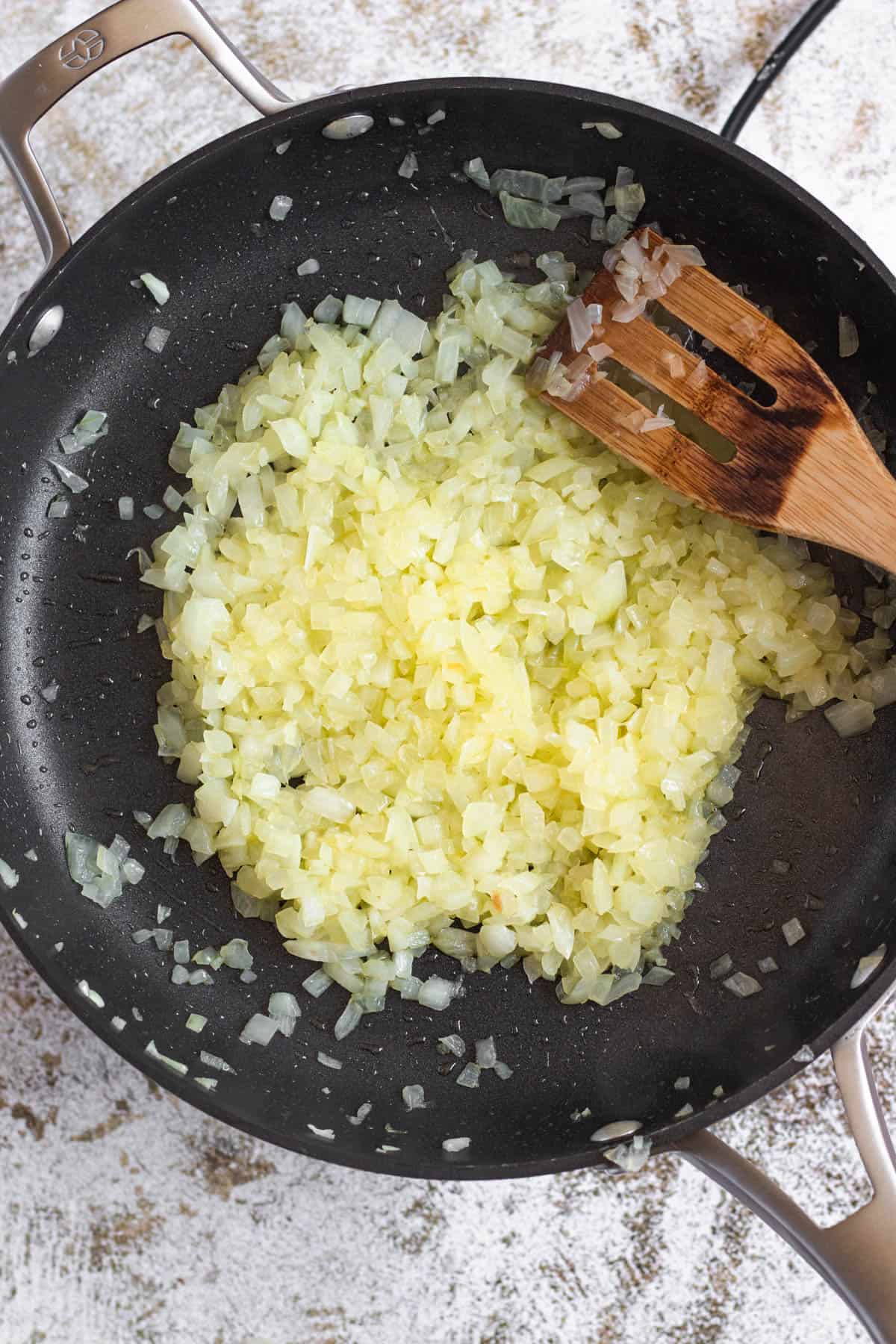 Sauteed onions in a pan with a wooden utensil