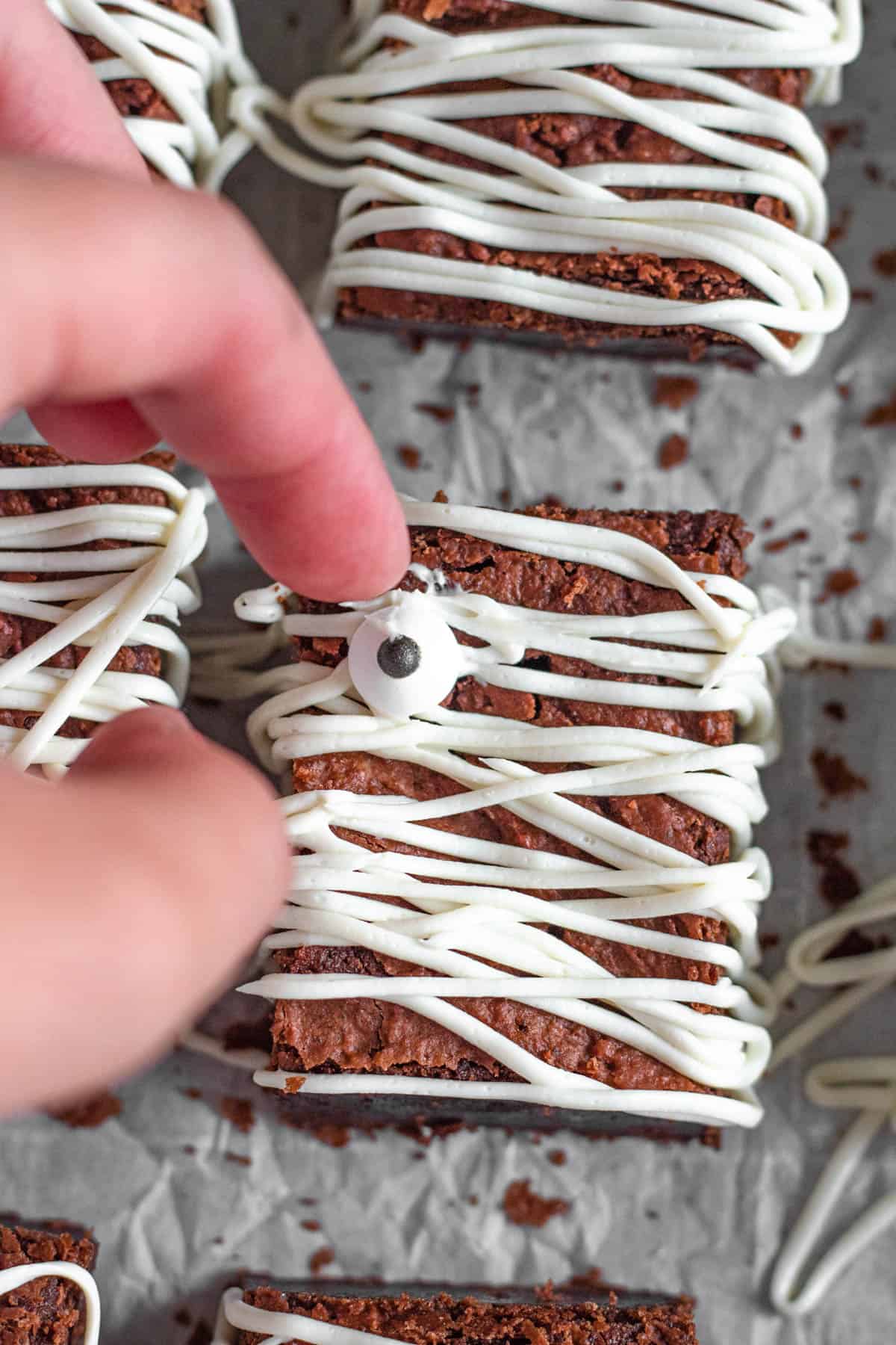 Fingers placing a candy eye on a frosting halloween brownie