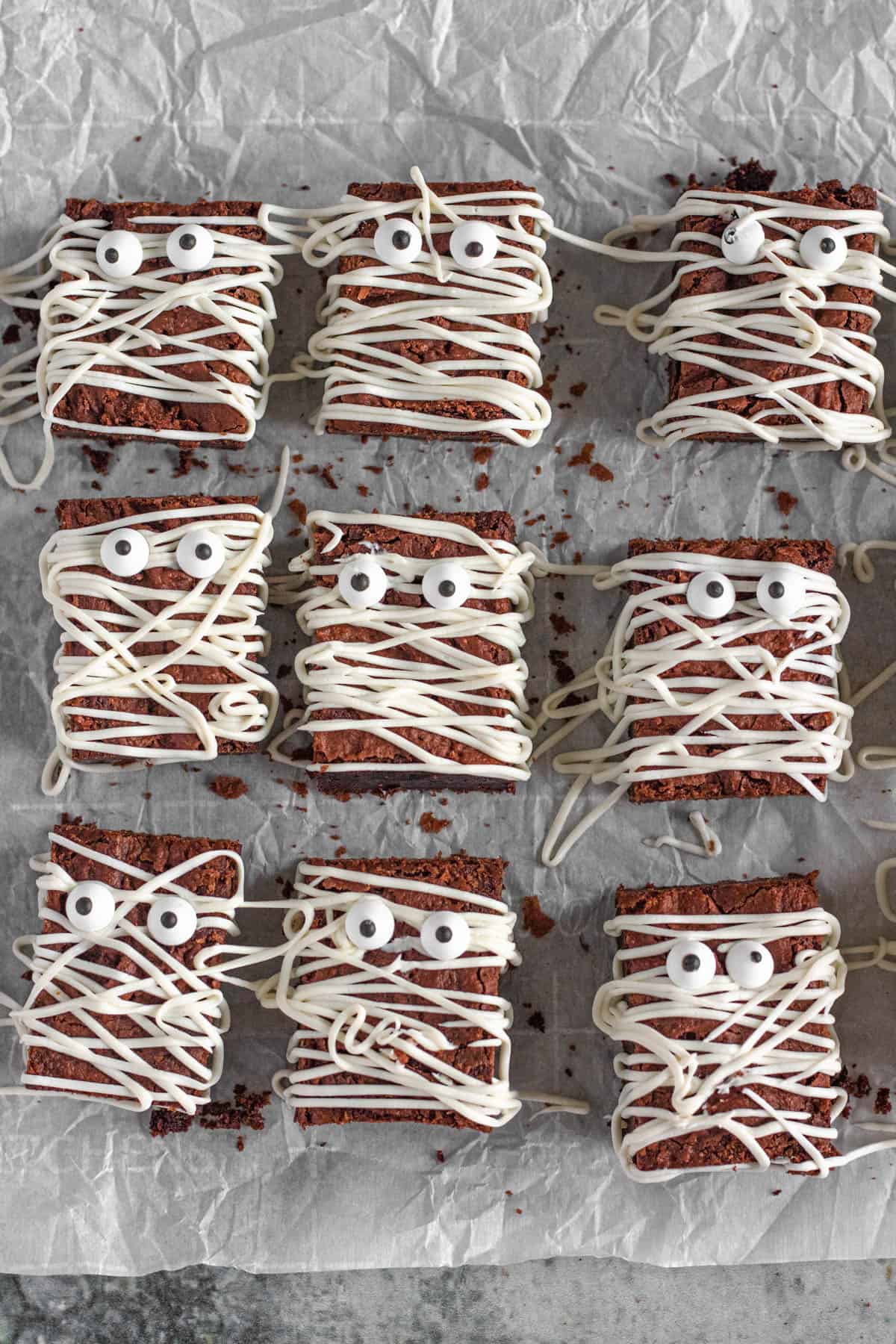9 Halloween brownies in the shape of mummies on parchment paper