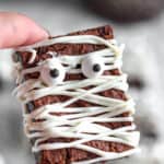 A hand holding mummy brownies with candy eyes.