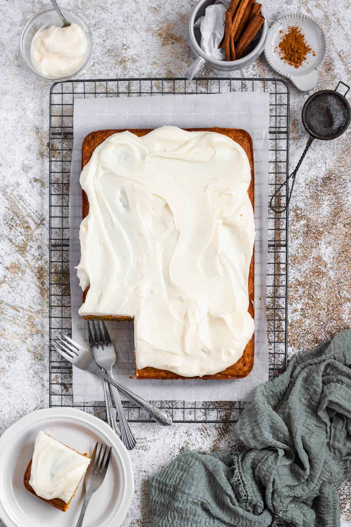 Cake on a cooling rack with cream cheese frosting with forks and a linen 
