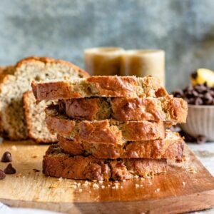 Slices of Banana bread piled high on a cutting board, surrounded by chocolate chips.