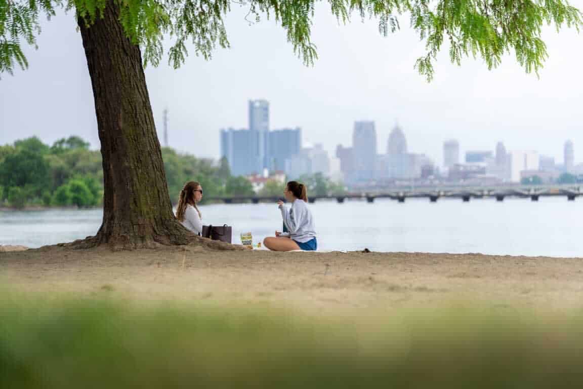 Two girls enjoying a picnic on the beach with a city in the background.