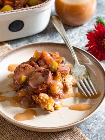 Apple Donut Bread Pudding served on a small plate and topped with vanilla sauce.