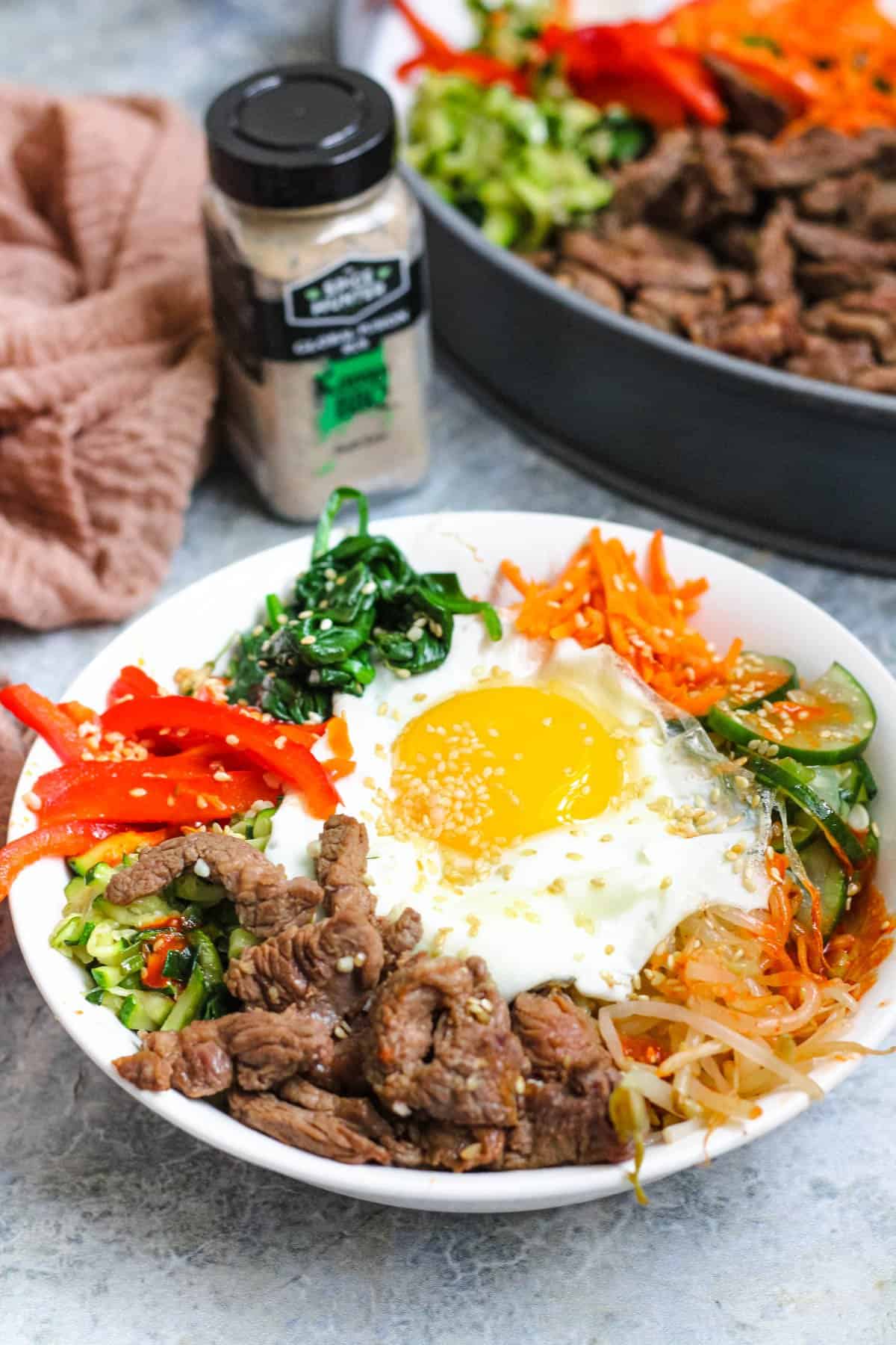 Bowl of bibimbap with a platter of vegetables behind it