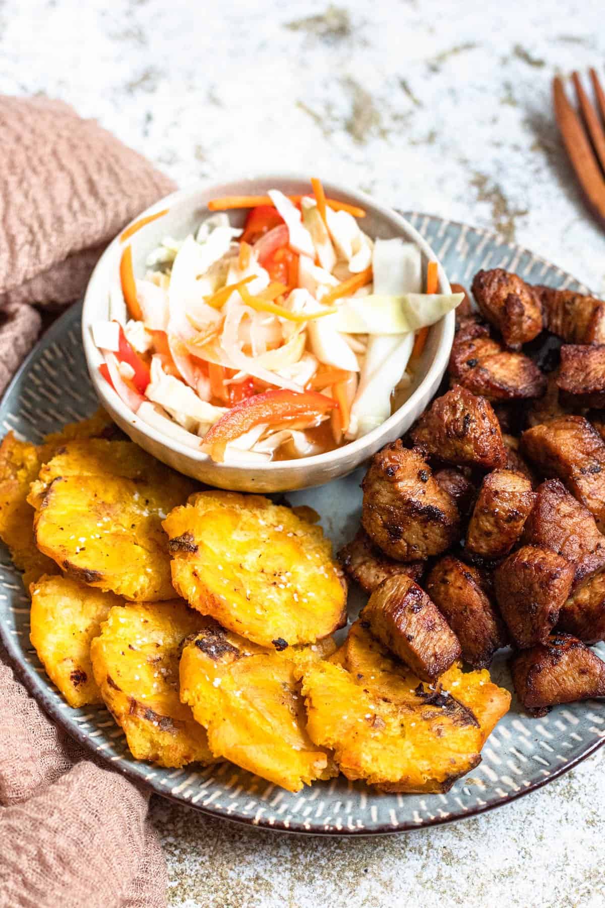 Haitian Griot on a plate with tostones and pikliz 