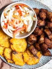 Haitian Griot on a plate next to Tostones and pikliz.