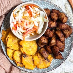 Haitian Griot on a plate next to Tostones and pikliz.