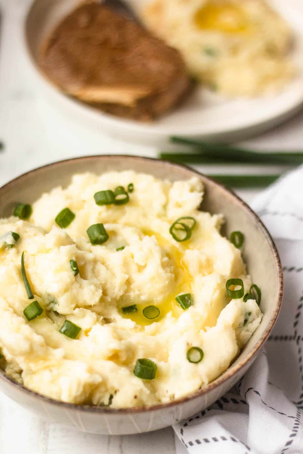 A bowl of horseradish mashed potatoes with butter on top and chopped green onions. 
