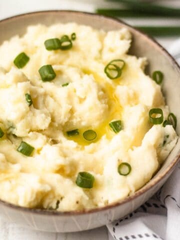 Bowl of horseradish mashed potatoes topped with melted butter and chopped green onions.