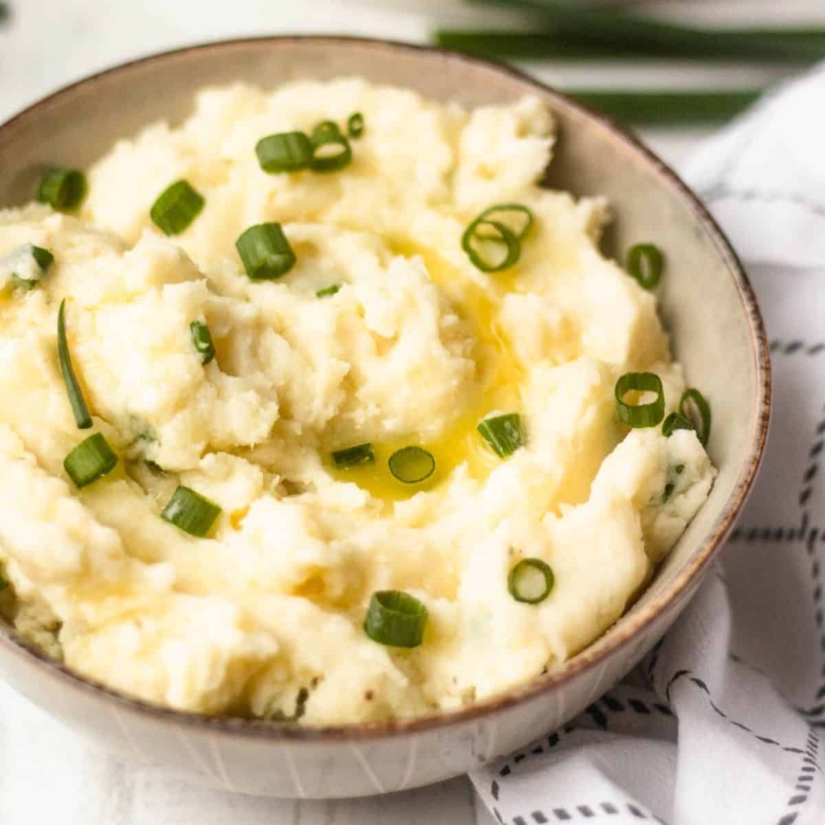 Bowl of horseradish mashed potatoes topped with melted butter and chopped green onions.