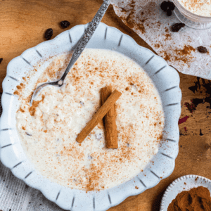 A bowl of arroz con leche topped with sprinkled cinnamon and cinnamon sticks.