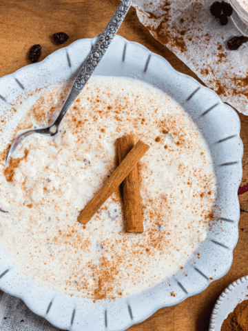 A bowl of arroz con leche topped with sprinkled cinnamon and cinnamon sticks.