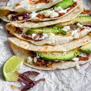 Baleadas on parchment paper with lime slices and red onions in front of it.